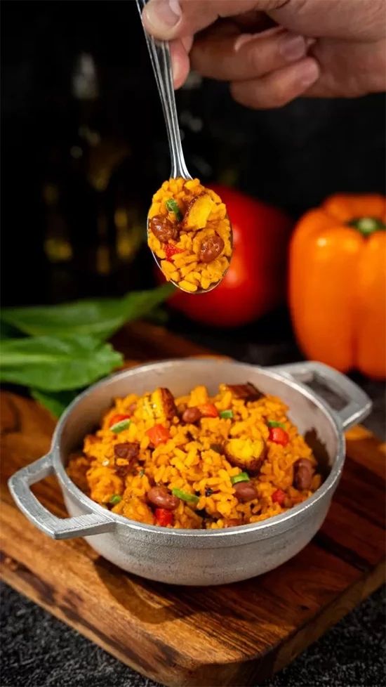 A spoon holds vibrant yellow rice with vegetables and meat over a rustic pot.